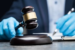 judge with medical gloves holds a gavel in right hand and writes with a pen in left hand