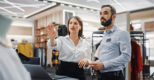 Manager shows employee how to operate computer system in retail store.