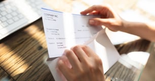 close up of hands pulling a paycheck out of an envelope.