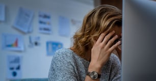 Tired woman holds her head in her hands while sitting at her desk in front of the computer