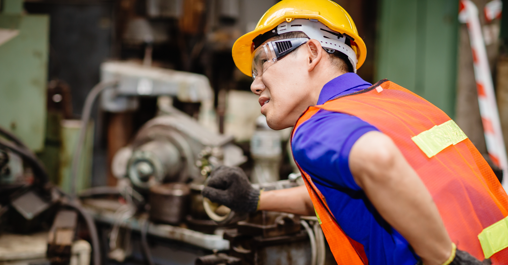 Machine worker is shown operating machine while bending over and holding his lower back with one hand. 