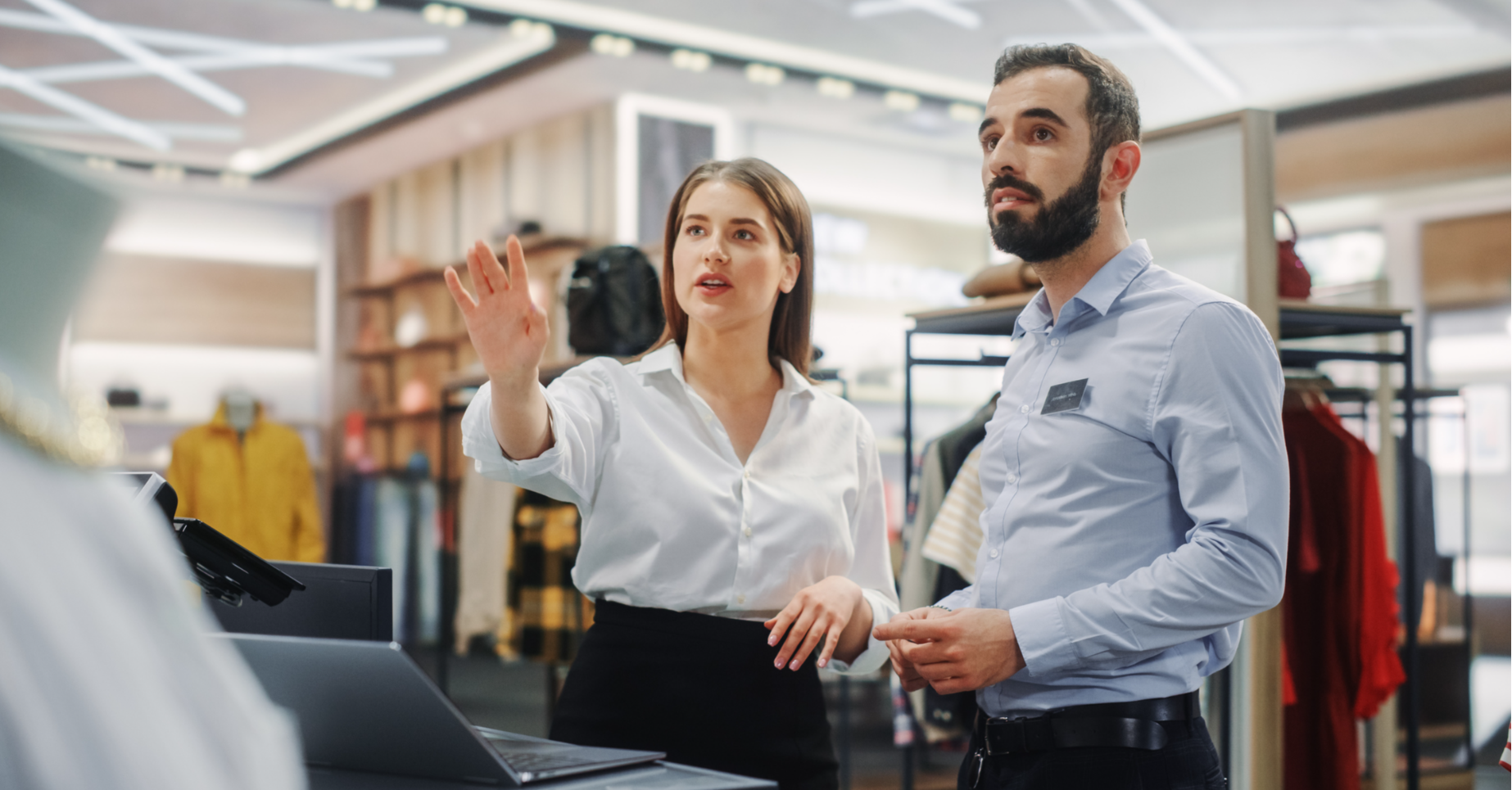 Manager shows employee how to operate computer system in retail store.