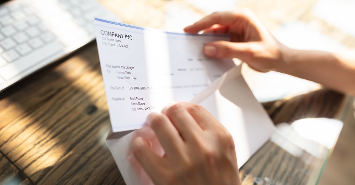 close up of hands pulling a paycheck out of an envelope.