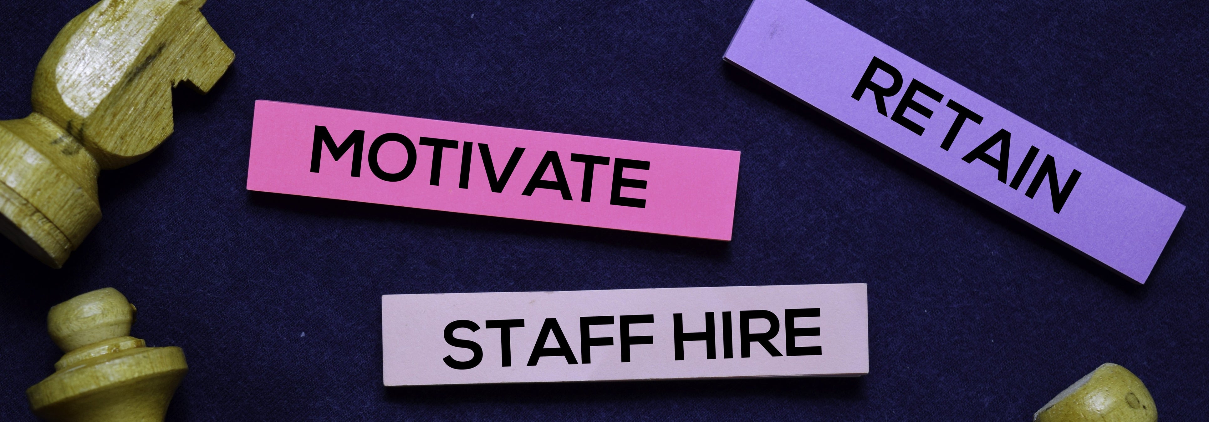 Chess pieces and blocks on table that say motivate, staff hire, and retain