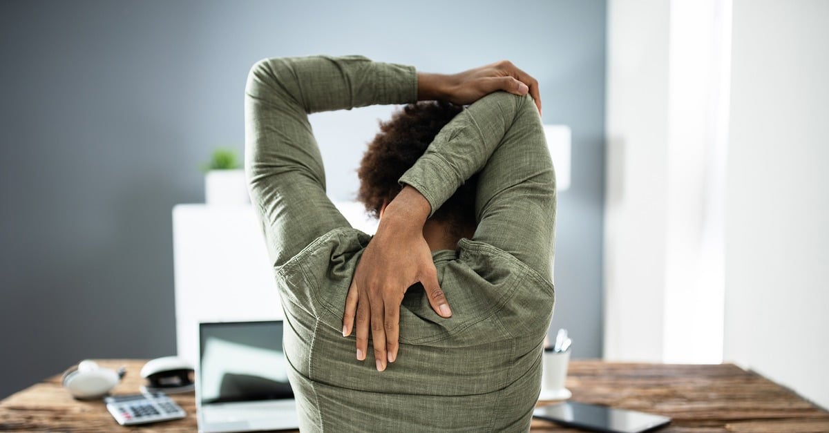 A woman sits down in a chair with her arm behind her head and stretches.