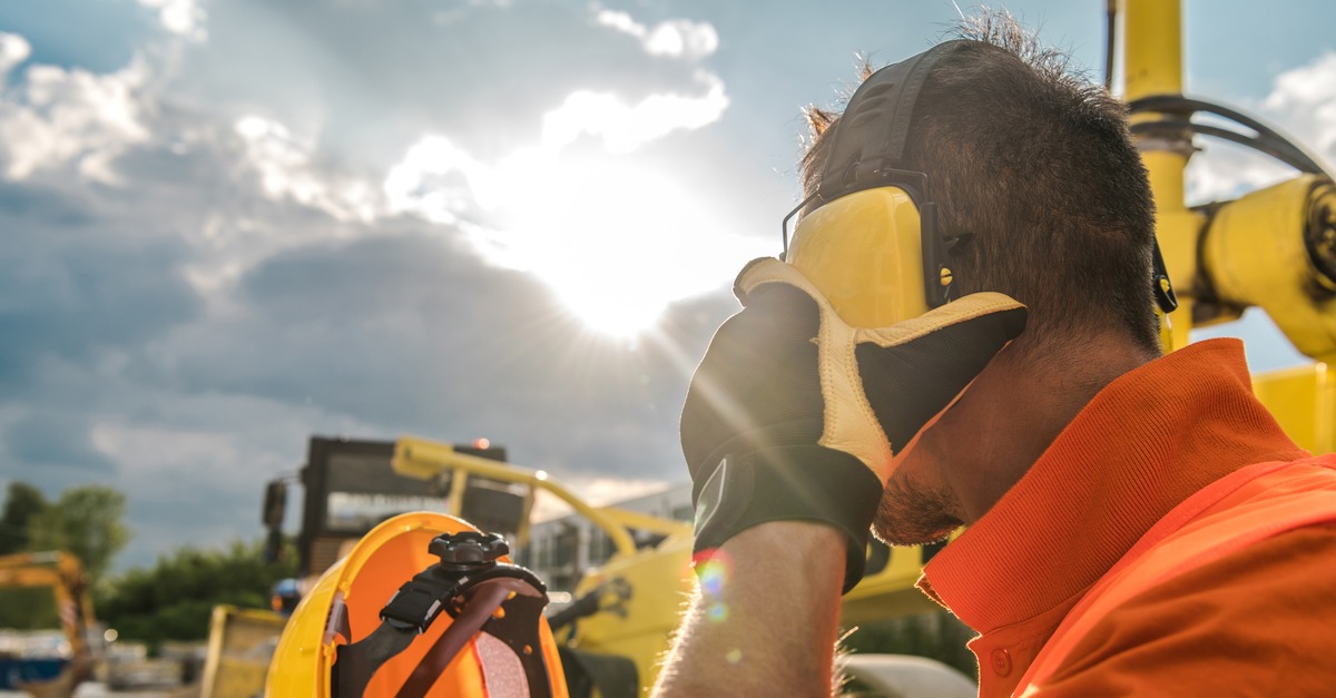 Construction worker places protective ear muffs over ears